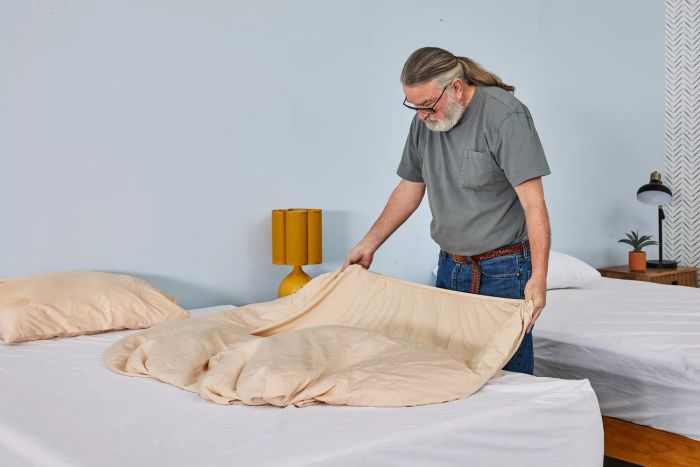 A person unfolding part of the Hush Iced Cooling Sheet Set on a mattress.
