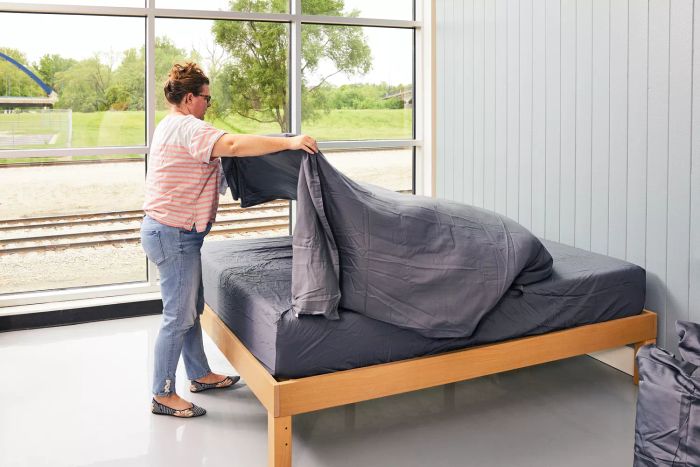A person is seen unfolding a Bampure 100% Organic Bamboo sheet over a mattress.