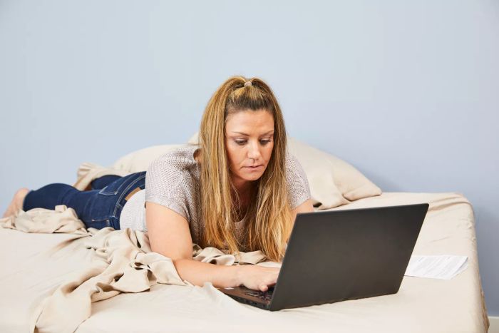 A person reclining on a bed dressed in The Company Store Company Cotton Rayon Made From Bamboo Sateen Sheet Set, with a laptop beside them.