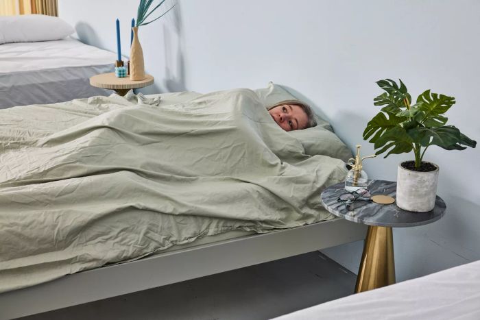 A person lying on the light green DreamFit DreamChill Collection Enhanced Bamboo Sheet Set with their eyes open.