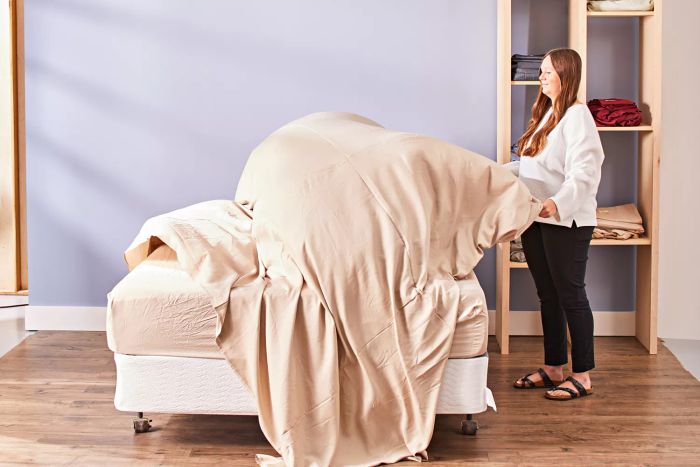 A person holding the top sheet of a Cozy Earth Bamboo Sheet Set over a mattress