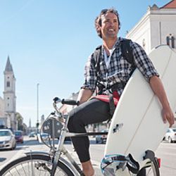 A man riding a bicycle while carrying a surfboard