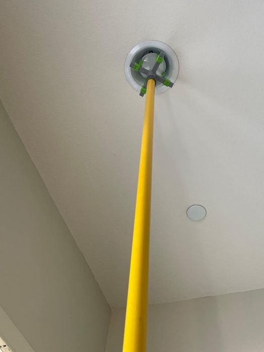 A yellow broom handle extended to adjust a white ceiling-mounted smoke detector