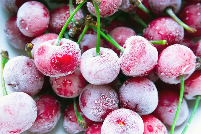 Frozen ripe cherries rest on a white surface, coated in frost.