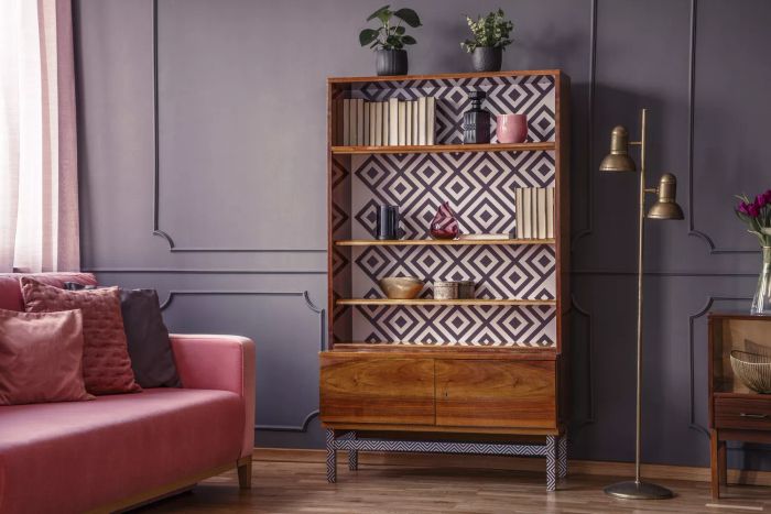 A revamped wooden bookshelf featuring a geometric design paired with a sleek brass floor lamp, set against a chic, dimly lit living room with a cozy pink sofa.