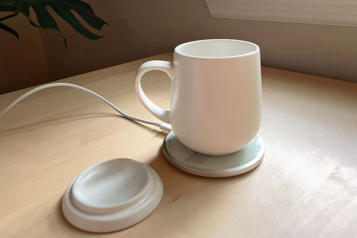 The Ohom Ui Self-Heating Mug Set showcased on a wooden table, connected to a power source
