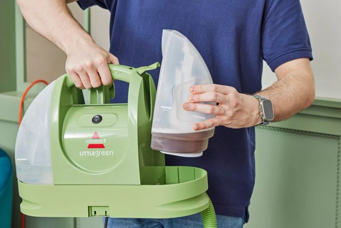 A person is taking out the dirty water tank from the Bissell Little Green Portable Carpet Cleaner.