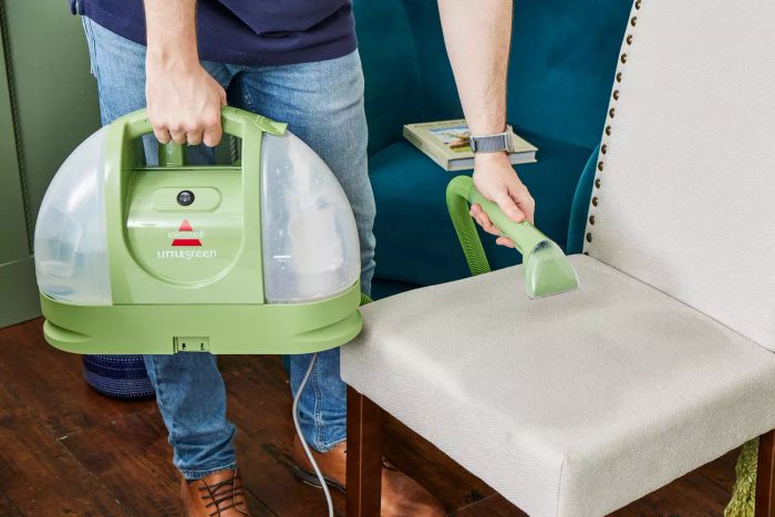 A person using the Bissell Little Green Portable Carpet Cleaner to clean a chair’s upholstery.