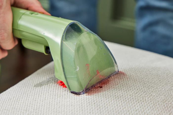 A close-up shot of the Bissell Little Green Portable Carpet Cleaner on a red stain