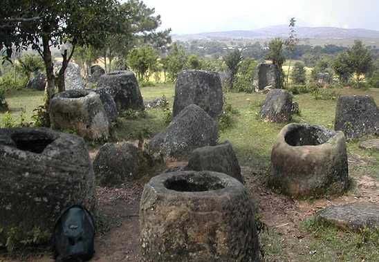 The Plain of Jars, located in Laos, is an ancient and mysterious archaeological site consisting of approximately 90 locations scattered across the Xieng Khouang Plateau. Each site houses jars that vary in number from one to four hundred. These large stone jars, believed to be created over 3,000 years ago, are made from a variety of materials such as sandstone, limestone, granite, breccia, and conglomerate, though sandstone is most common. The tallest jar stands at about 9 feet. At first glance, the jars seem randomly positioned, but closer examination reveals that their arrangement aligns with the patterns of stars in the constellations. The purpose of these jars remains speculative, with hypotheses ranging from serving as drinking vessels for a giant race, to being used for rainwater collection, or even as burial urns. A few jars have been discovered to contain bodies, tools, or miniature Buddha statues. However, the site remains dangerous due to unexploded bombs left over from the Secret War.