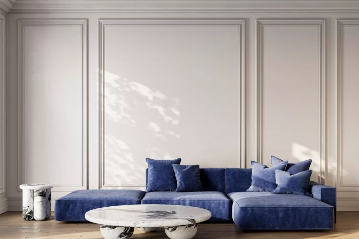 A modern white interior featuring a plush blue velour sofa, sleek marble coffee tables, and elegant moldings. Illustrated in a 3D render mockup.