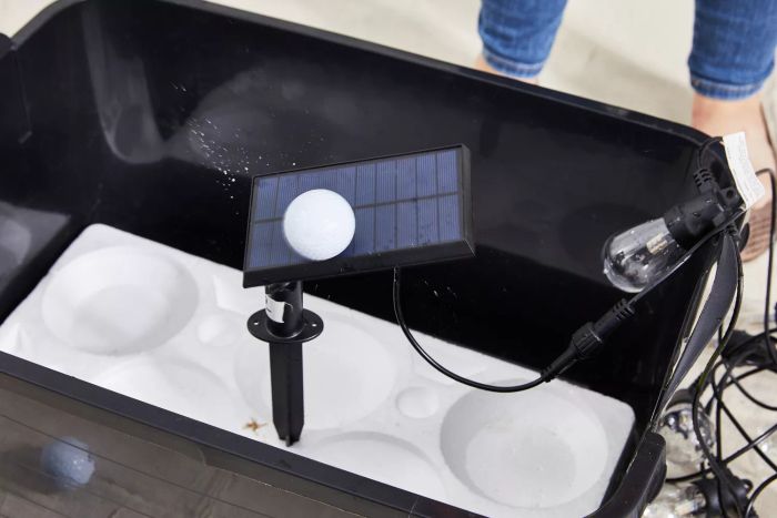 A golf ball falling onto the Brightech Ambiance Pro Solar Non-Hanging String Lights, placed in a black bucket