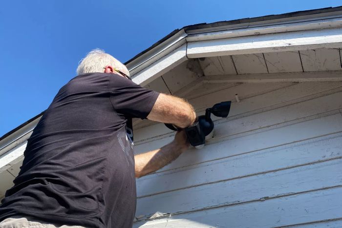 An individual sets up the Ring HD Motion-Activated Floodlight Camera on the outside of their home.