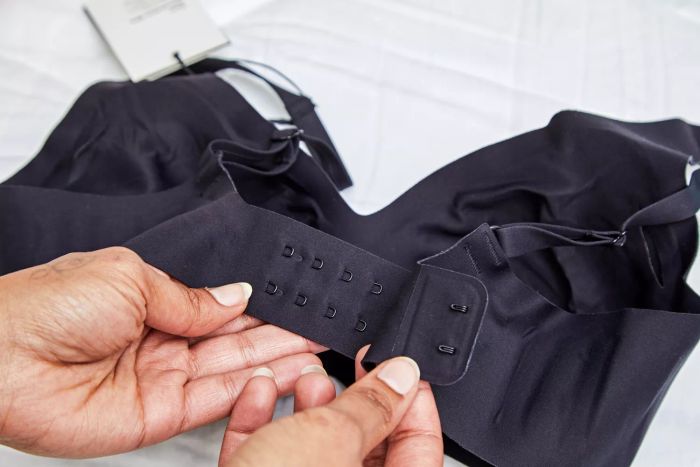 A person is fastening the hooks at the back of the Knix Revolution V-Neck Bra.