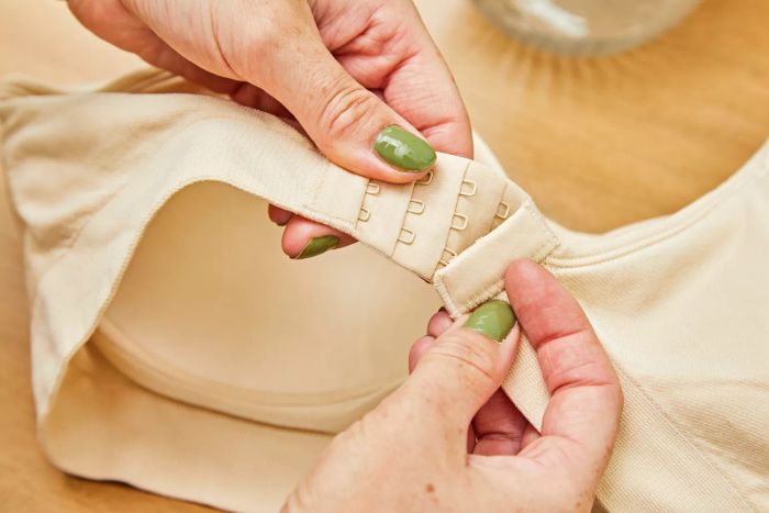 A person is fastening the hooks at the back of the Underoutfit The Comfort Shaping Bra.
