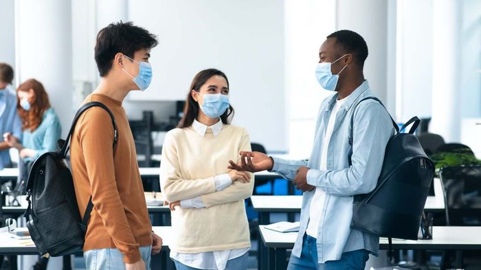 A group of teenagers conversing while wearing masks.