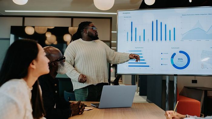 A professional is displaying graph data on a large screen to a group of colleagues in a meeting room.