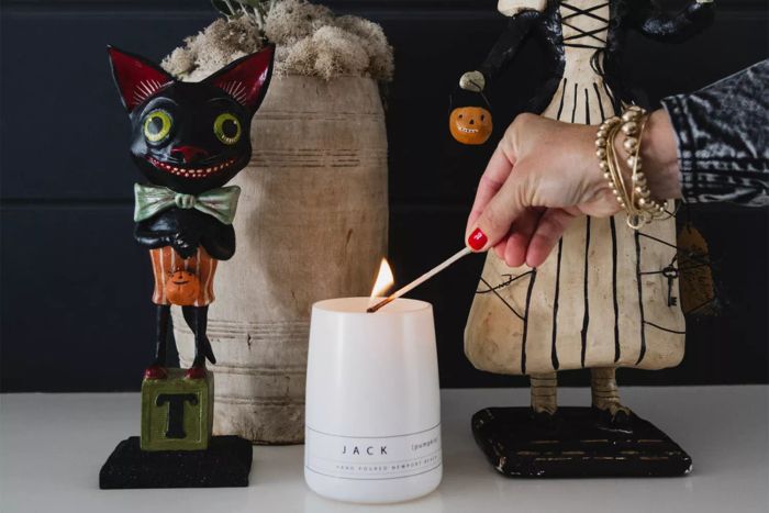 A pumpkin-themed candle on a table surrounded by Halloween decorations.