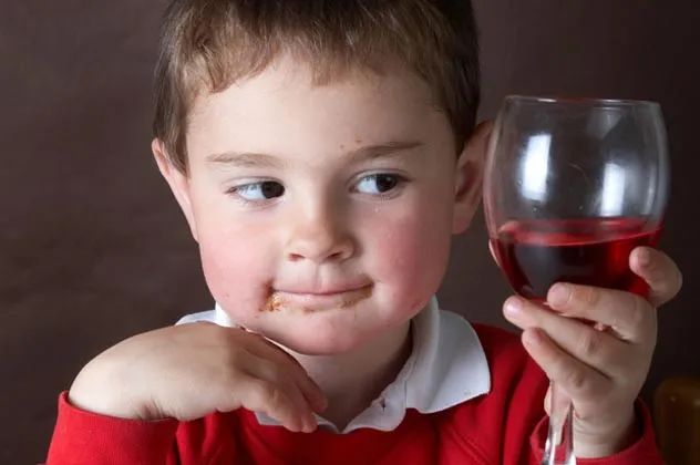 A young boy with a glass of red wine