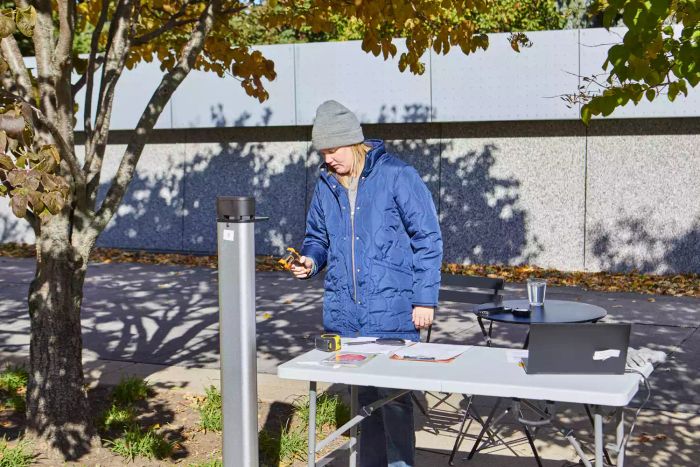 Person using a thermometer to measure the temperature of the EnerG+ Electric Patio Heater beside a table with a laptop outdoors.