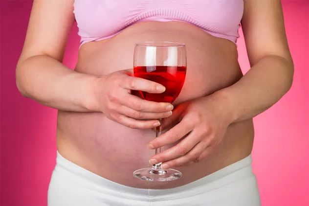 A pregnant woman holding a glass of red wine
