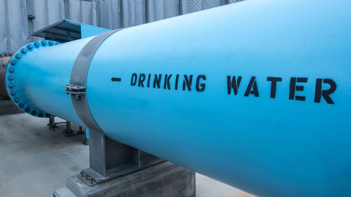 Water from a desalination plant flows through a large, blue pipe ready for consumption.