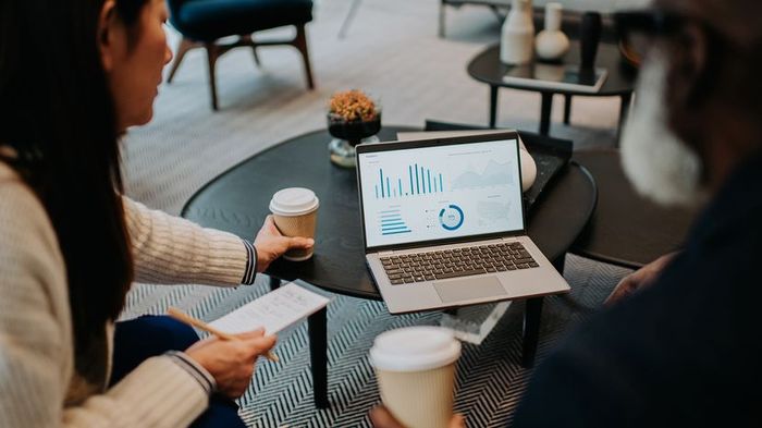 A group of colleagues casually meets on a sofa with coffee and a laptop in hand