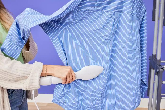 A person smoothing out a blue shirt with the NORI Press Iron while it hangs