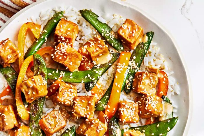 This crispy peanut tofu dish, paired with vibrant sugar snap peas and peppers, brings a delightful crunch to the table.
