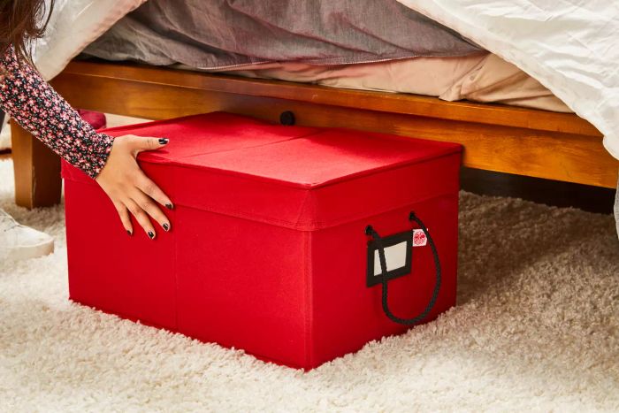 A person is shown placing the Santa's Bags 3-Drawer Christmas Ornament Storage Box (72 Ornaments) beneath a bed