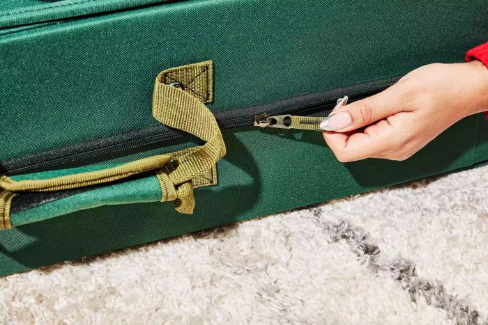 A hand is grasping the zipper of the Treekeeper Gift Wrap Craft Station.