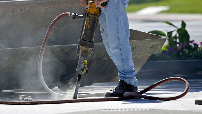A man operating a power drill on concrete.