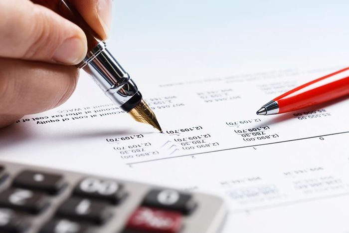 A hand holding a pen, annotating an accounting ledger.