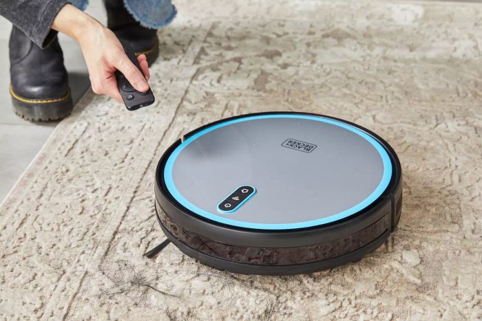 A hand holding the remote control for the Black + Decker RoboSeries Robot Vacuum
