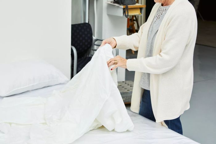 A person making a bed with the Crane & Canopy Soft White 400 Thread Count Sheet Set