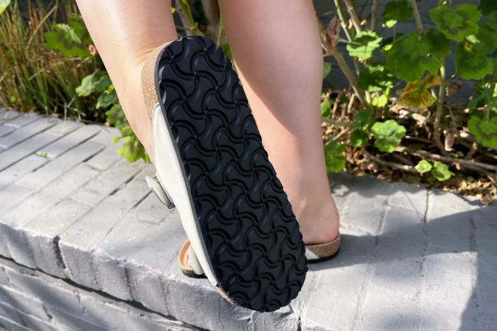 A person lifts their foot to display the sole of the Quince Nappa Leather Double Buckle Slides.