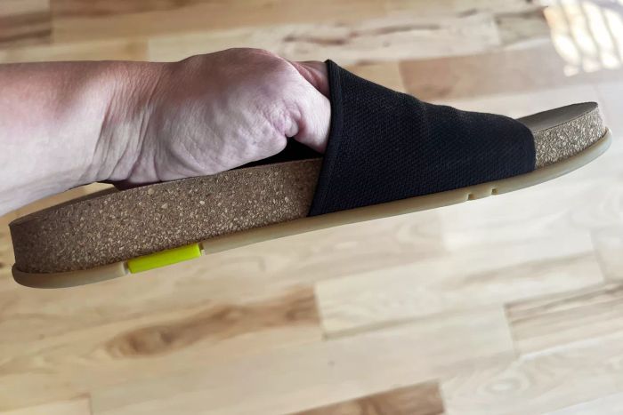 A person holding the Message Mullen Slide to display the side profile of the shoe.