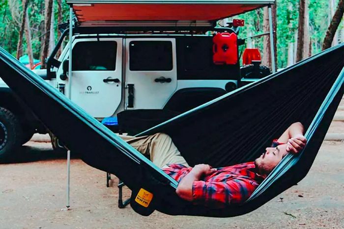 A person relaxing in a Wise Owl Outfitters Camping Hammock with Tree Straps at a campsite.