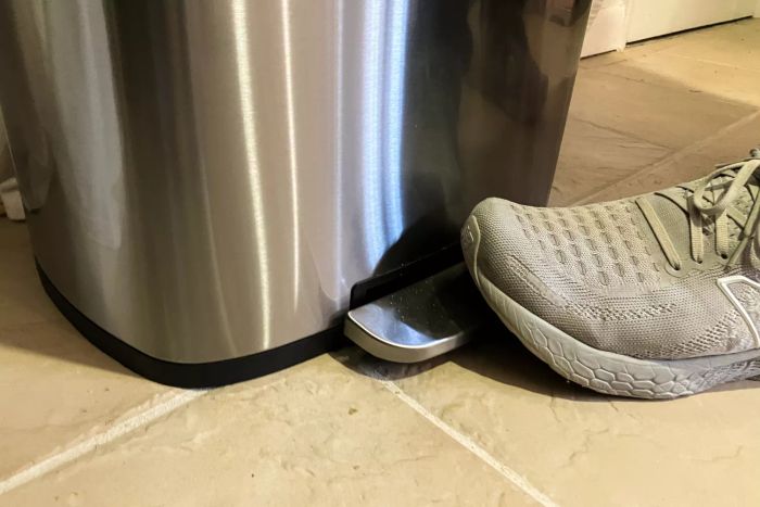 A person stepping on the foot pedal of the Amazon Basics 13.2 Gallon Soft-Close Trash Can with Foot Pedal