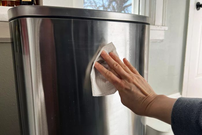 A person cleaning the exterior of the FDW 13 Gallon Kitchen Step Trash Can