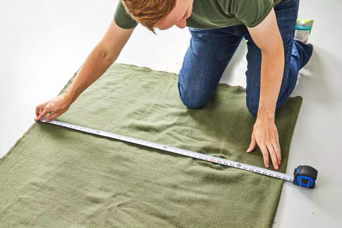 A person measuring the Faribault Mill Pure & Simple Wool Blanket on the floor