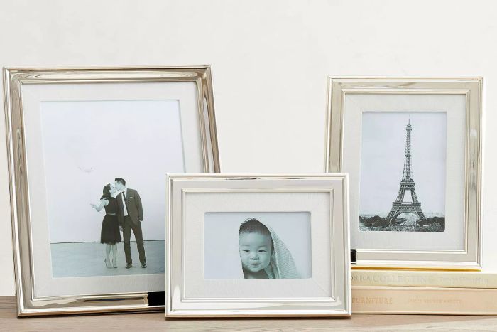Pictures framed in the Pottery Barn Personalized Silver-Plated Grosgrain Ribbon Mat Frame placed on a table.