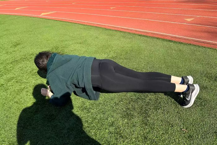 An individual performs a yoga pose on grass wearing the Spanx Booty Boost Active 7/8 Leggings