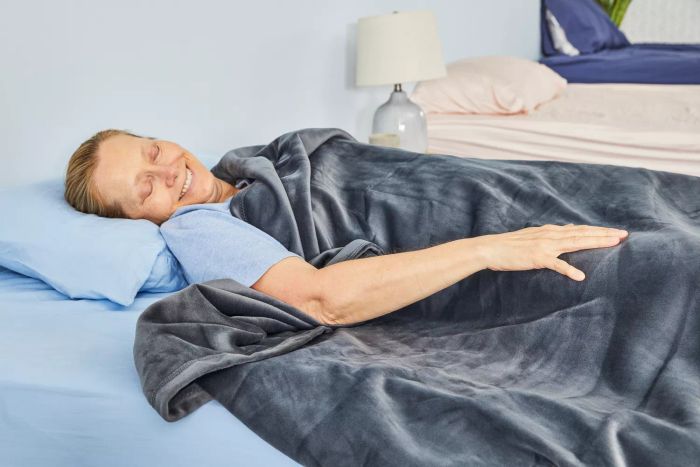 A person lying in bed, covered by the Big Blanket Co. Original Stretch Blanket