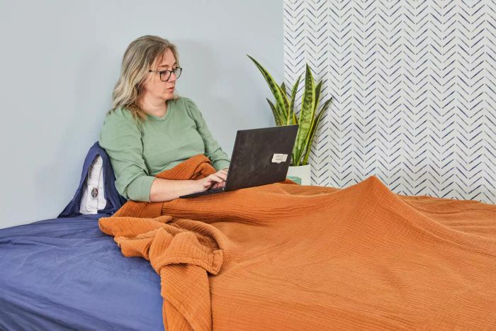 A person browsing the internet from the comfort of their bed, wrapped in the soft Quince Organic Airy Gauze Blanket