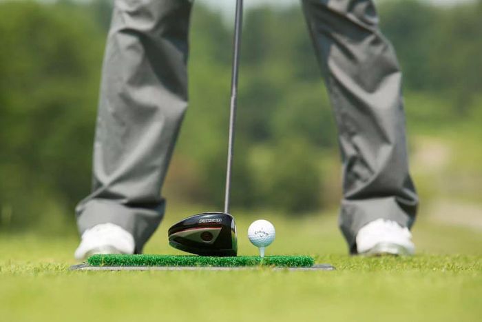 A close-up of the Callaway Golf Launch Zone Hitting Mat, with a driver positioned behind a golf ball placed on a tee on the green.
