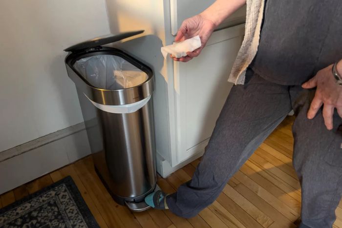 A person pressing the foot pedal of the Simplehuman 12 Gallon Slim Hands-Free Kitchen Step Trash Can