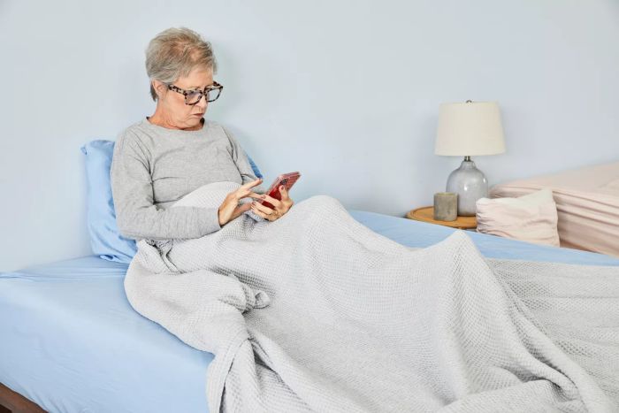 A person lying in bed, covered by the Boll & Branch Waffle Bed Blanket, while scrolling on their phone