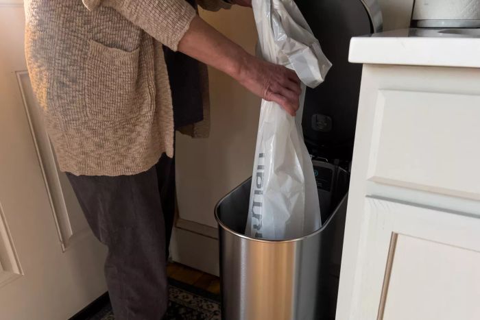 A person inserting a trash bag into the Simplehuman 12 Gallon Slim Hands-Free Kitchen Step Trash Can