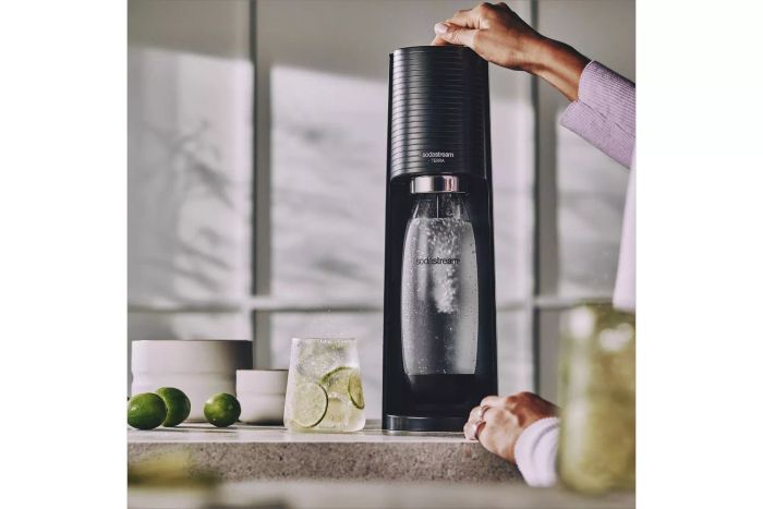 A person using the SodaStream Terra Sparkling Water Maker to carbonate water, with lime slices placed nearby for added flavor.